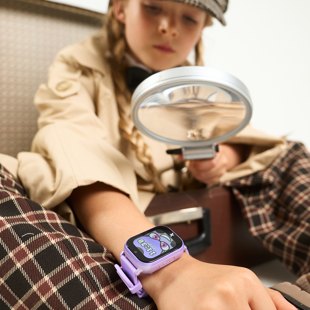 Dziewczynka w stroju detektywa ogląda smartwatch FW49 Kiddo 2 przez lupę