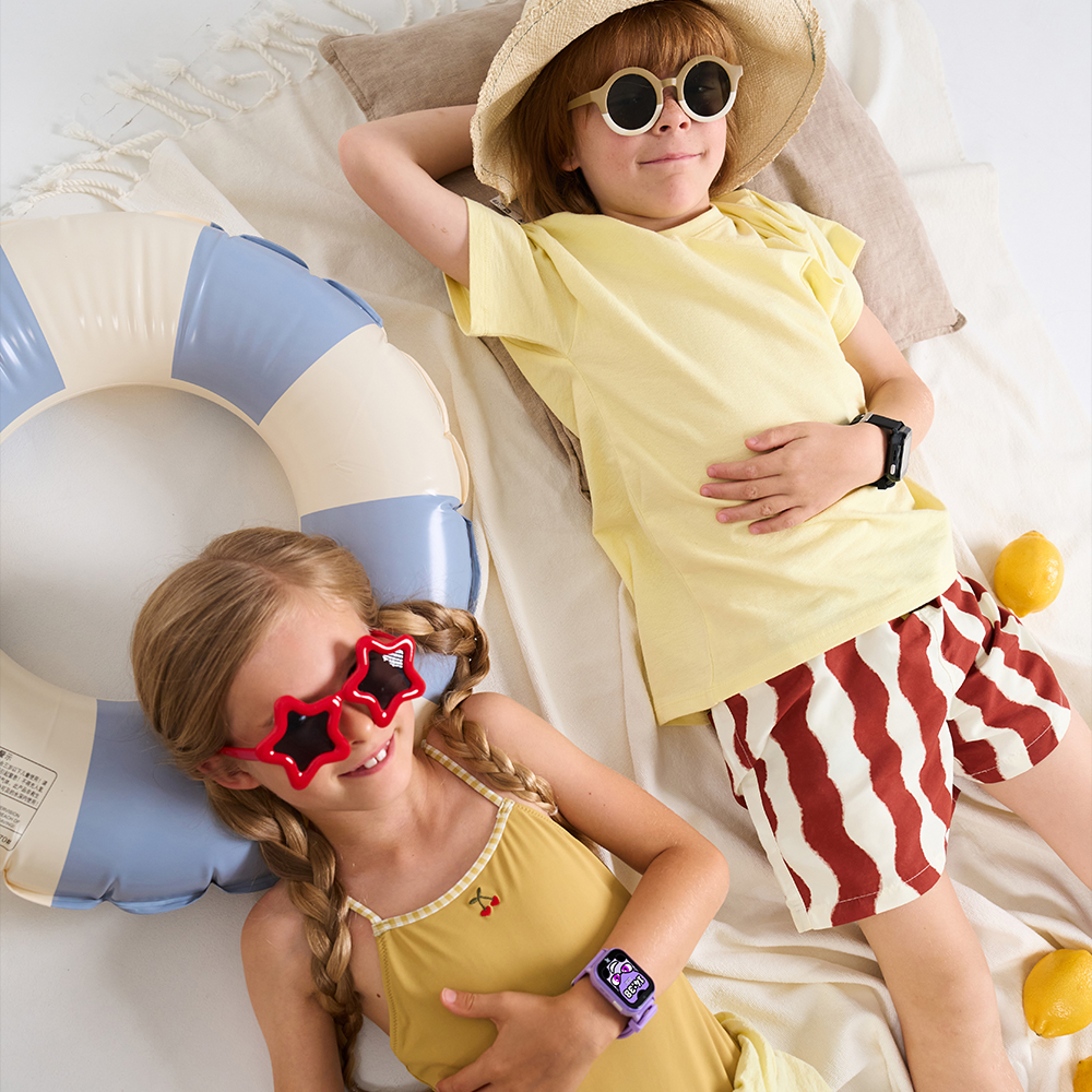 Chłopiec i dziewczynka w strojach plażowych i smartwatchach FW49 Kiddo 2 leżą na ręczniku i kole dmuchanym