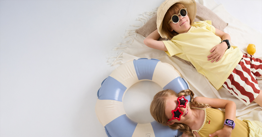 Chłopiec i dziewczynka w strojach plażowych i smartwatchach FW49 Kiddo 2 leżą na ręczniku i kole dmuchanym