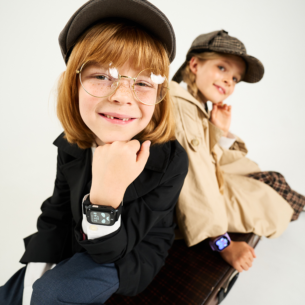 Chłopiec i dziewczynka w przebraniach detektywów patrzą w obiektyw kamery, na nadgarstkach mają smartwatche FW49 Kiddo 2