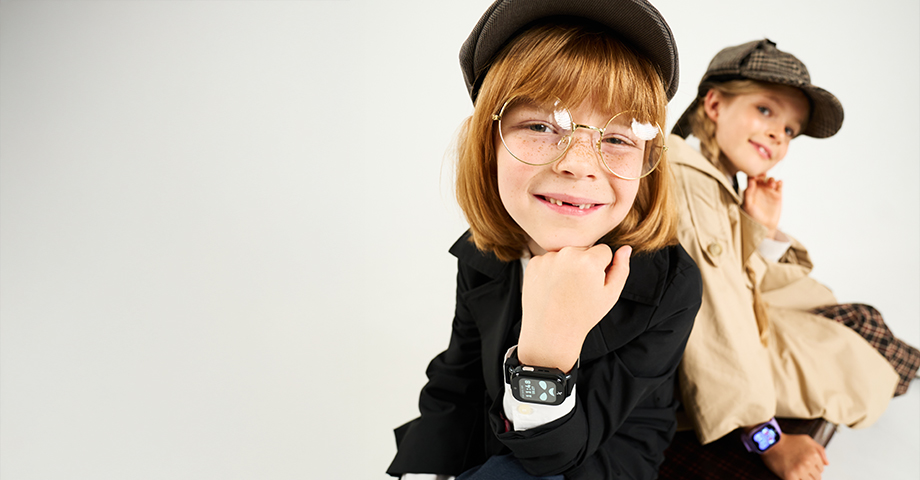 Chłopiec i dziewczynka w przebraniach detektywów patrzą w obiektyw kamery, na nadgarstkach mają smartwatche FW49 Kiddo 2