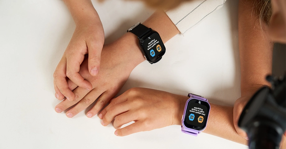 Widok z góry na dziecięce ręce ze smartwatchami FW49 na nadgarstkach - na obu uruchomiona funkcja 'Przyjaciele'.