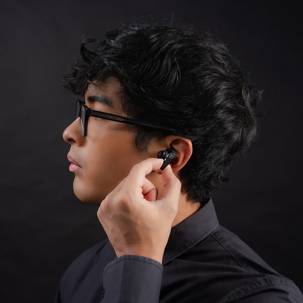 Mężczyzna w czarnej koszuli wkładający słuchawkę JLab Go Pods ANC do ucha.