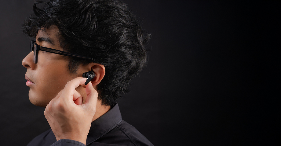 Mężczyzna w czarnej koszuli wkładający słuchawkę JLab Go Pods ANC do ucha.