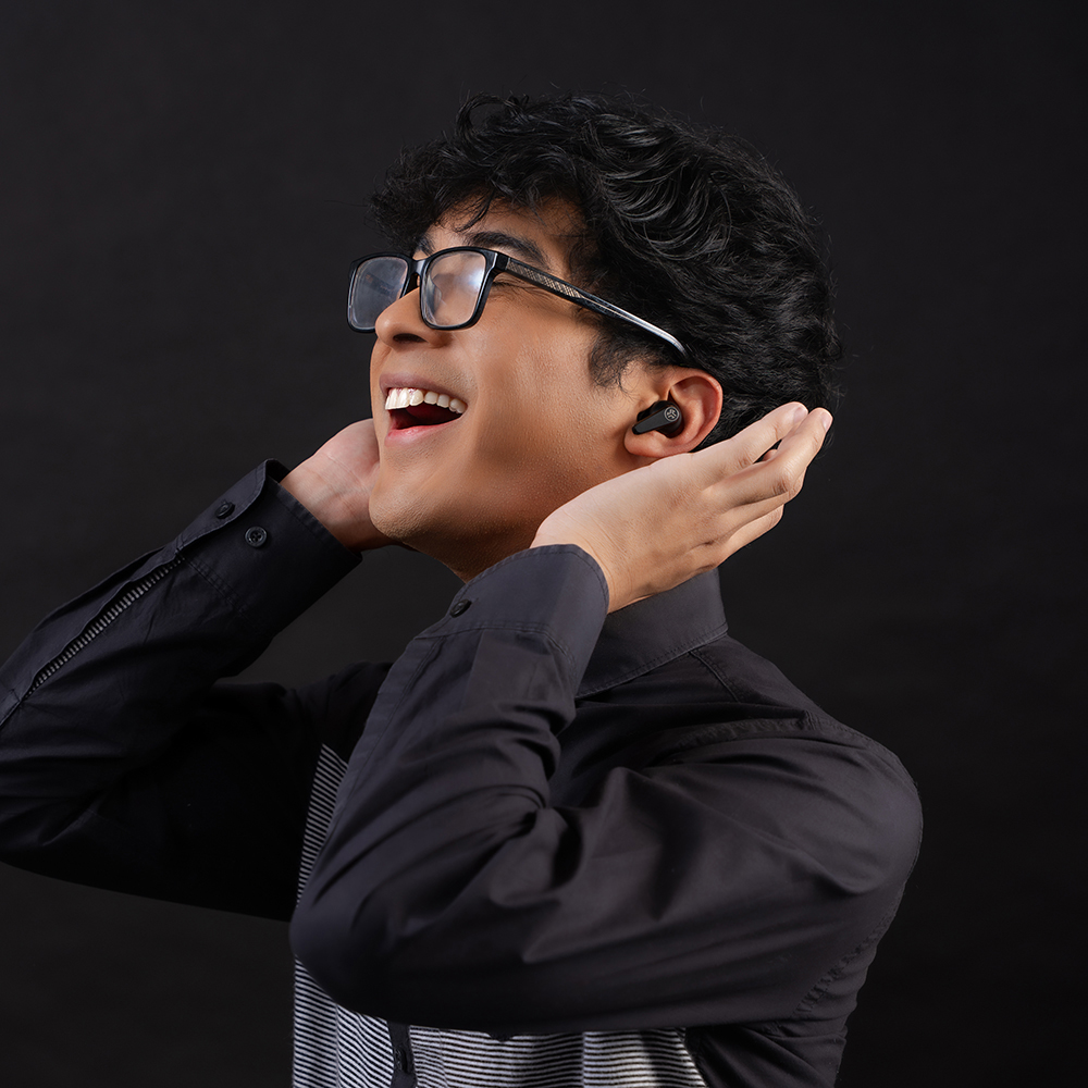 Mężczyzna w czarnej koszuli i okularach słuchający muzyki w słuchawkach JLab Go Pods ANC.