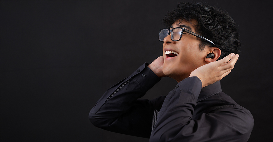 Mężczyzna w czarnej koszuli i okularach słuchający muzyki w słuchawkach JLab Go Pods ANC.