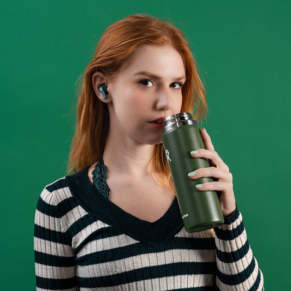 Kobieta z zielonym bidonem w słuchawkach JLab Go Pods ANC.