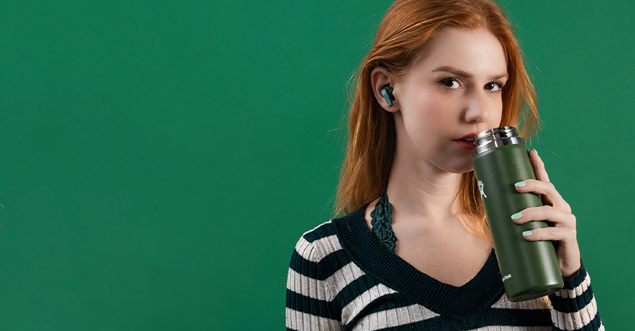 Kobieta z zielonym bidonem w słuchawkach JLab Go Pods ANC.