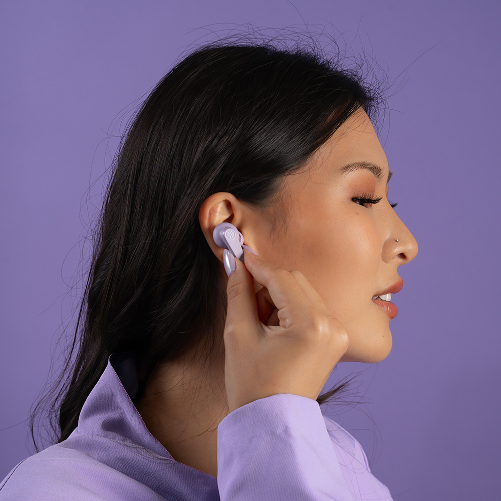 Kobieta w fioletowej marynarce wkładająca słuchawkę JLab Go Pods ANC do ucha.