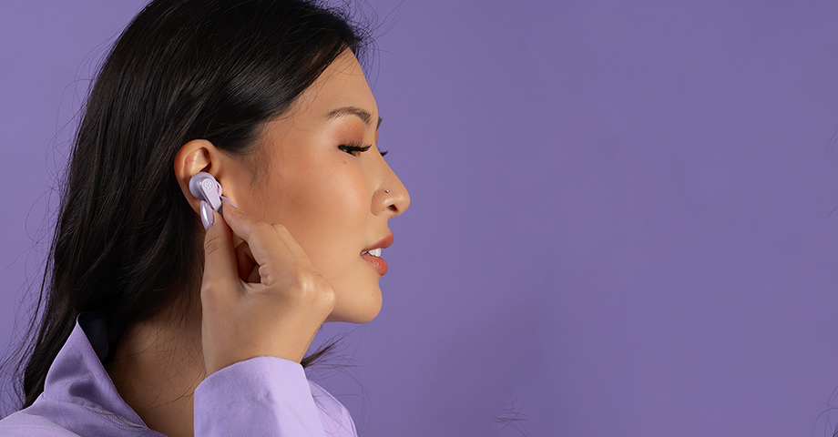 Kobieta w fioletowej marynarce wkładająca słuchawkę JLab Go Pods ANC do ucha.
