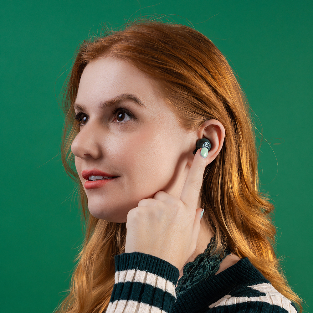 Kobieta w swetrze w zielone-białe paski wkładająca słuchawkę JLab Go Pods ANC do ucha.