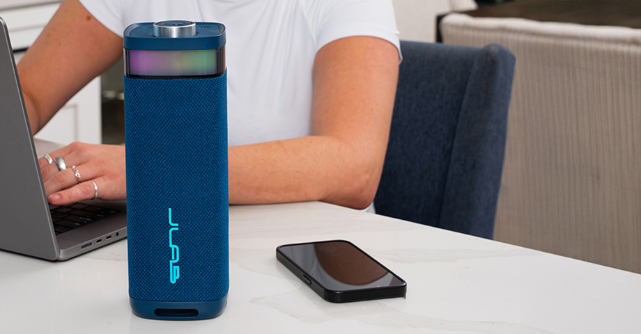 Niebieski JLab JBuds Party na stole obok laptopa i smartfonu.