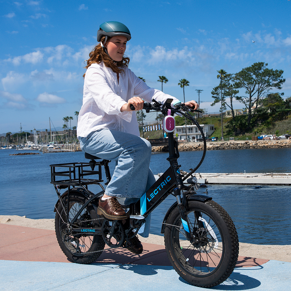 Kobieta na rowerze elektrycznym z przypiętym głośnikiem JLab Pop Party.