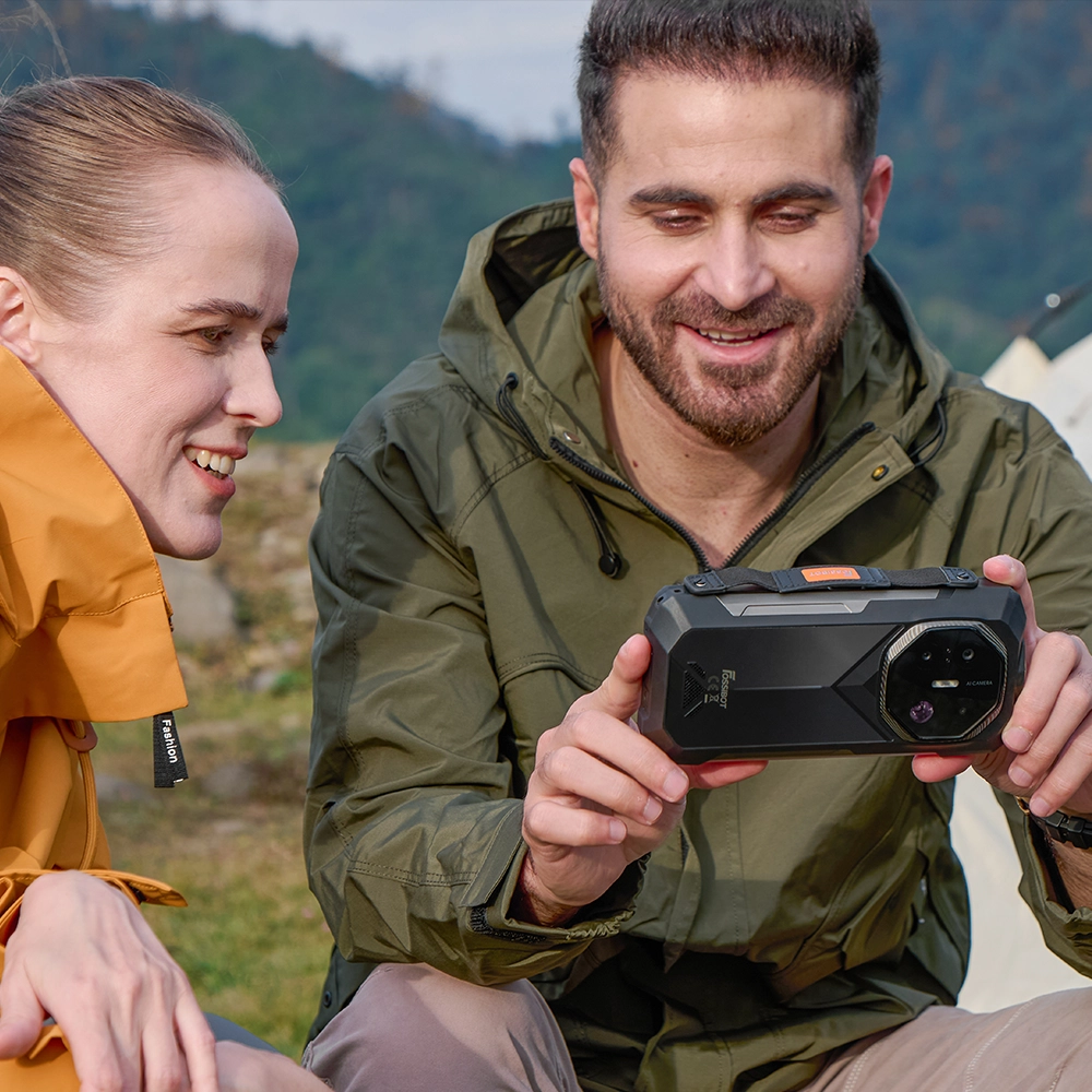 Zbliżenie na mężczyznę trzymającego Fossibot F113 5G poziomo i pokazującego na nim coś kobiecie siedzącej obok.