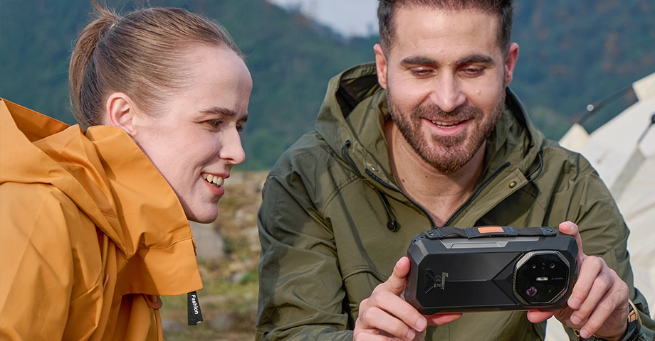 Mężczyzna trzymający Fossibot F113 5G poziomo i pokazujący coś na nim kobiecie siedzącej obok.