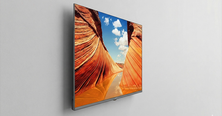 Telewizor AIWA 43 UHD zawieszony na szarej ścianie.