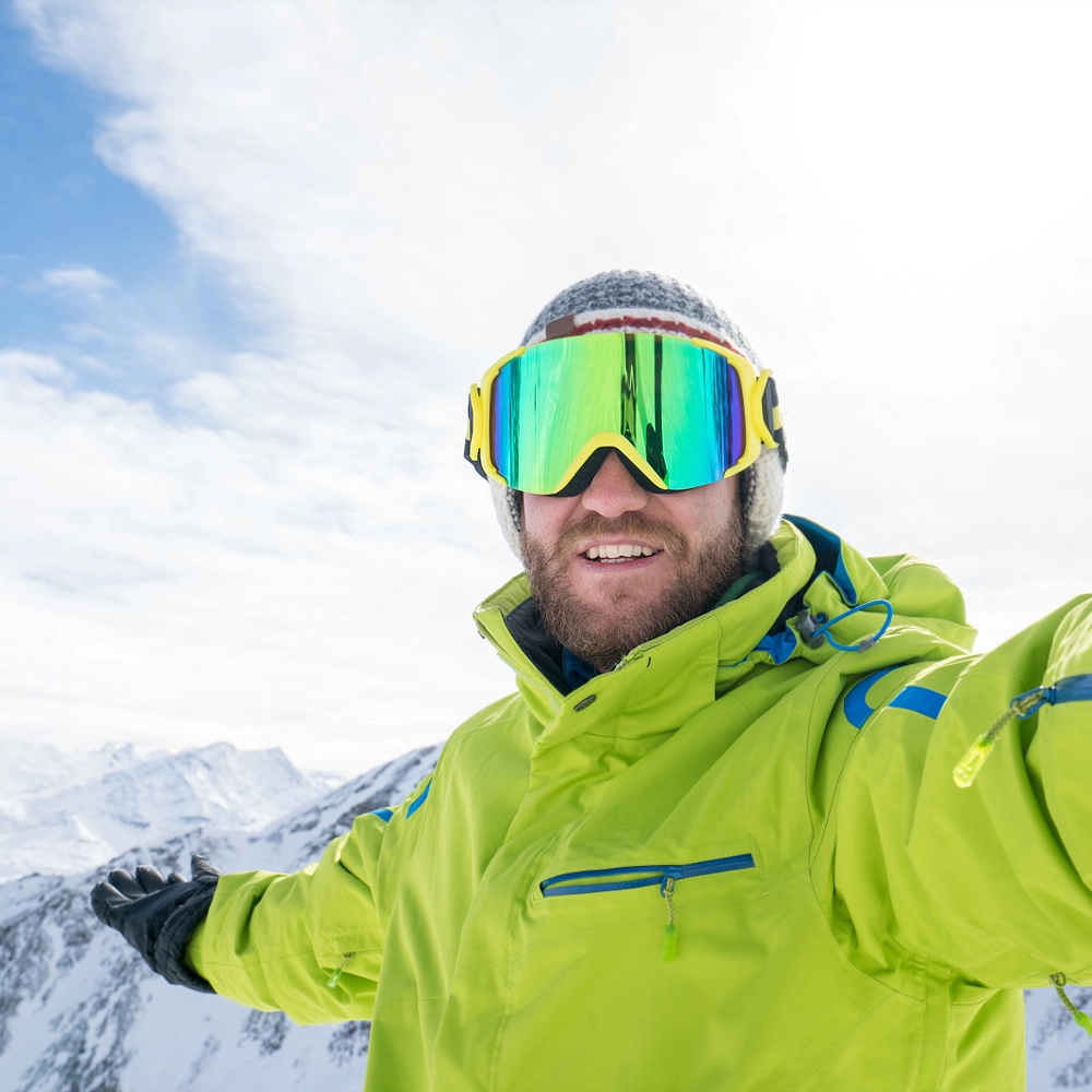 Zbliżenie na mężczyznę w zimowym ubraniu robiącego sobie zdjęcie na tle wysokich, ośnieżonych gór.