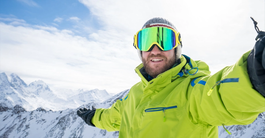 Mężczyzna w zimowym ubraniu robiący sobie zdjęcie na tle wysokich, ośnieżonych gór.