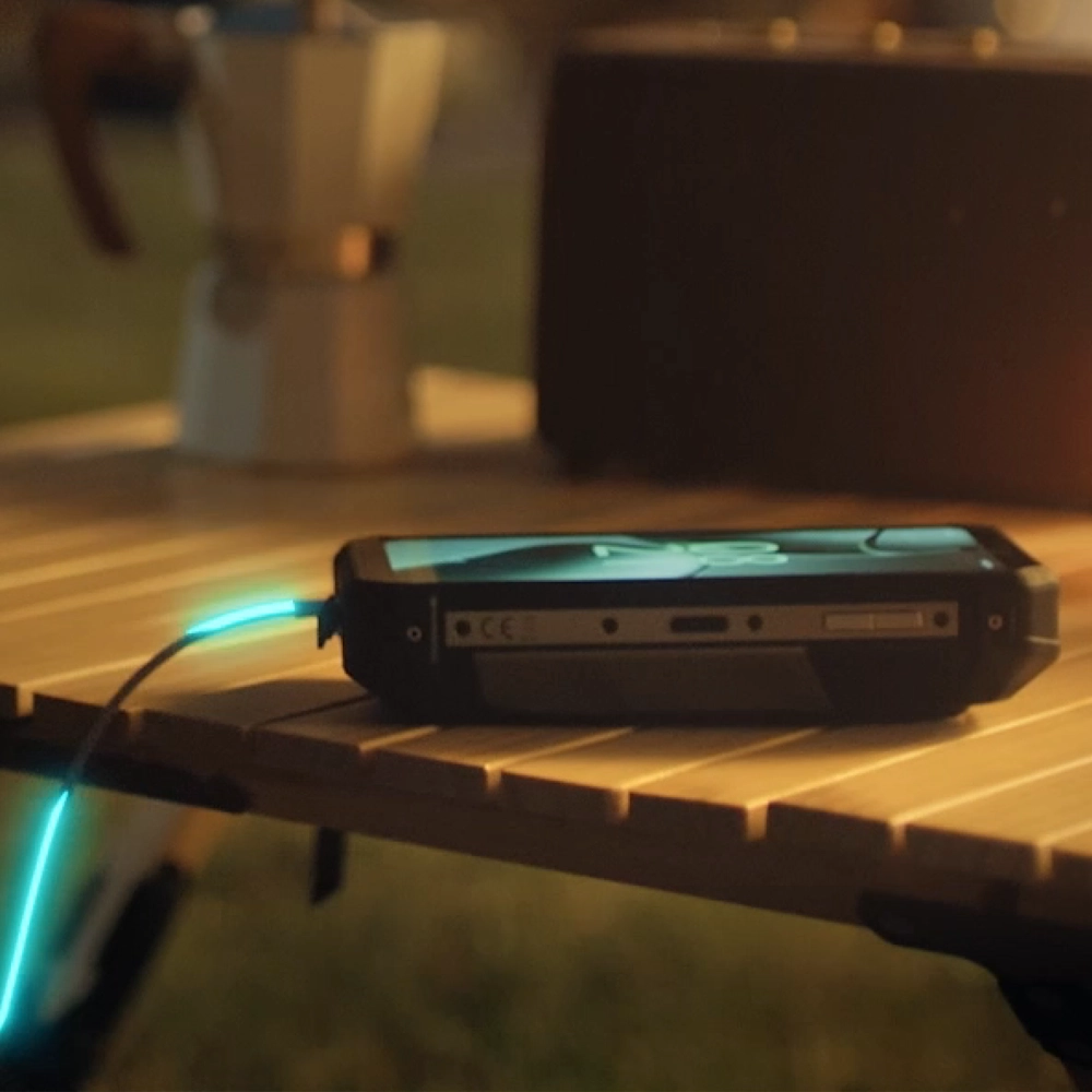 Zbliżenie na telefon Fossibot F107 podłaczony do przewodu ładującego na stoliku ogrodowym.