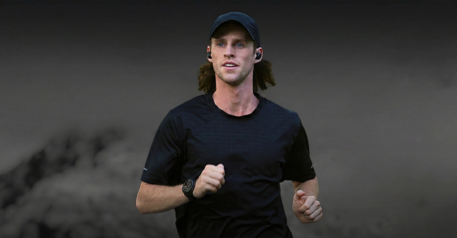 Mężczyzna w sportowej koszulce i czapce z daszkiem biegnący w słuchawkach i ze smartwatchem Kospet Tank T4 na nadgarstku.