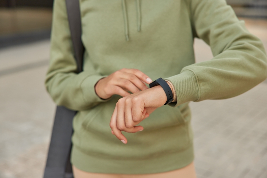 Smartwatch na nadgarstku osoby w zielonej bluzie na zewnątrz.