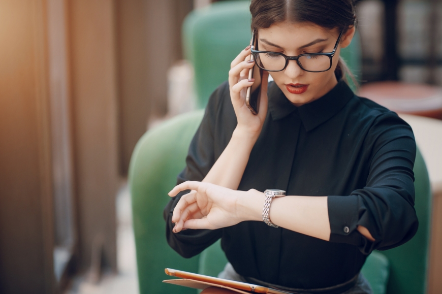Elegancko ubrana kobieta rozmawiająca przez telefon sprawdza czas na smartwatchu