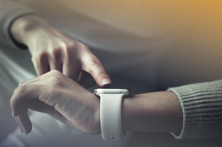 Osoba w szarym swetrze obsługująca smartwatch za pomocą palca wskazującego