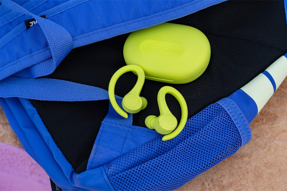 Limonkowe słuchawki JLAB Go Air Sport z etui leżące na niebieskim plecaku sportowym.
